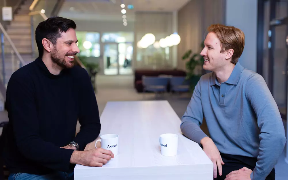 Två manliga medarbetare på Axfoods kontor ler mot varandra