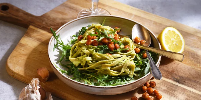 En skål med pasta, ruccola och kikärter i.